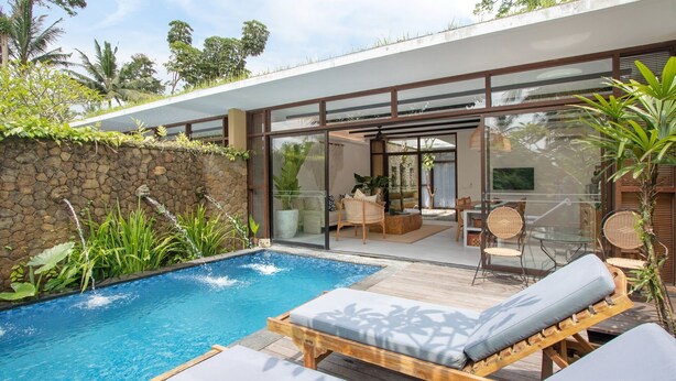 Uma área de piscina moderna ao ar livre, com espreguiçadeiras, uma parede de pedra e um terraço envidraçado.