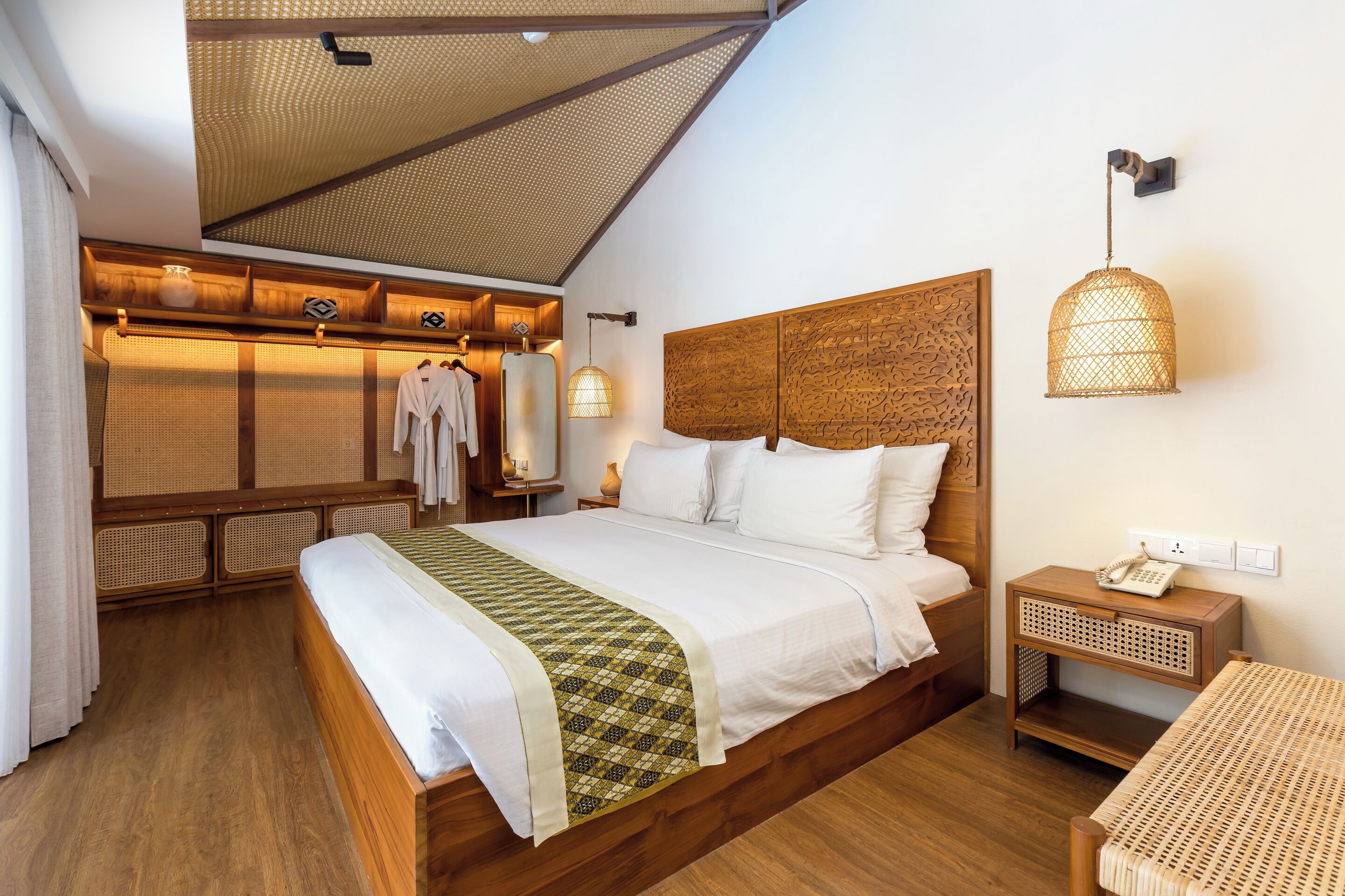 Un dormitorio con una cama de madera, una mesita de noche con una lámpara y un banco tejido.