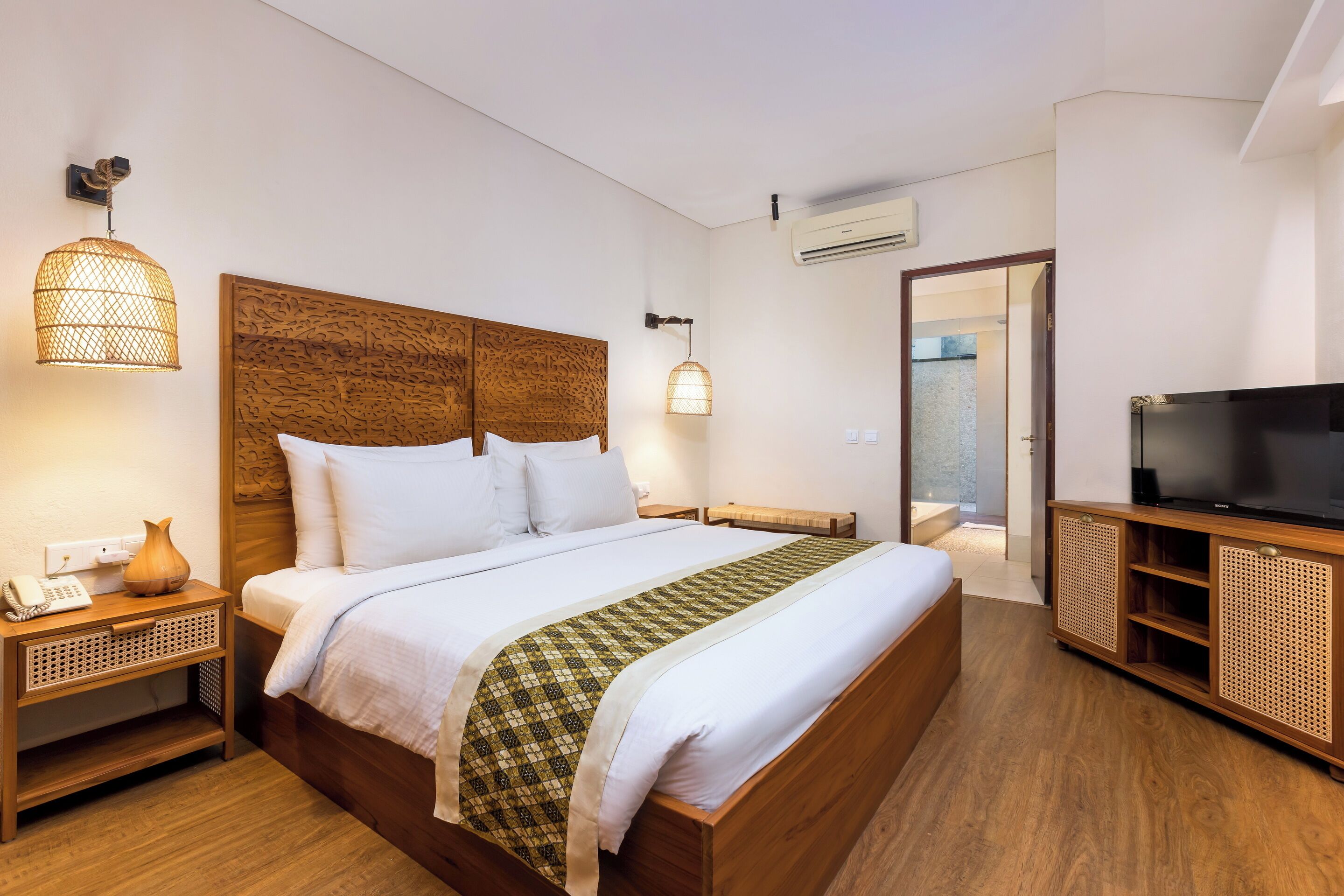 Una habitación de hotel ordenada con una cama grande, lámparas de noche, un televisor y un cabecero de madera.