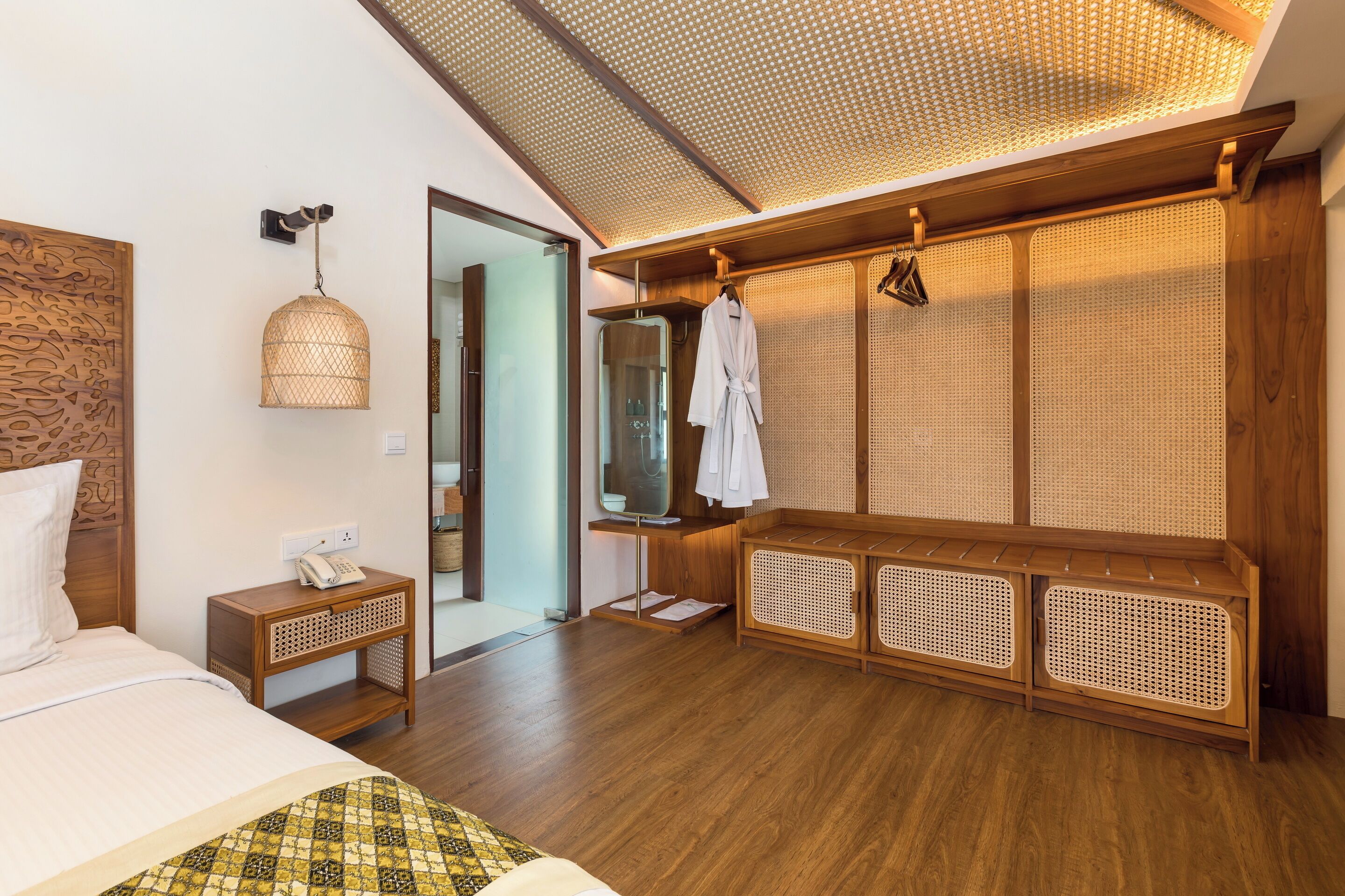 A modern hotel room with a wooden bed, a bedside telephone, a hanging light fixture, and a large mirror.