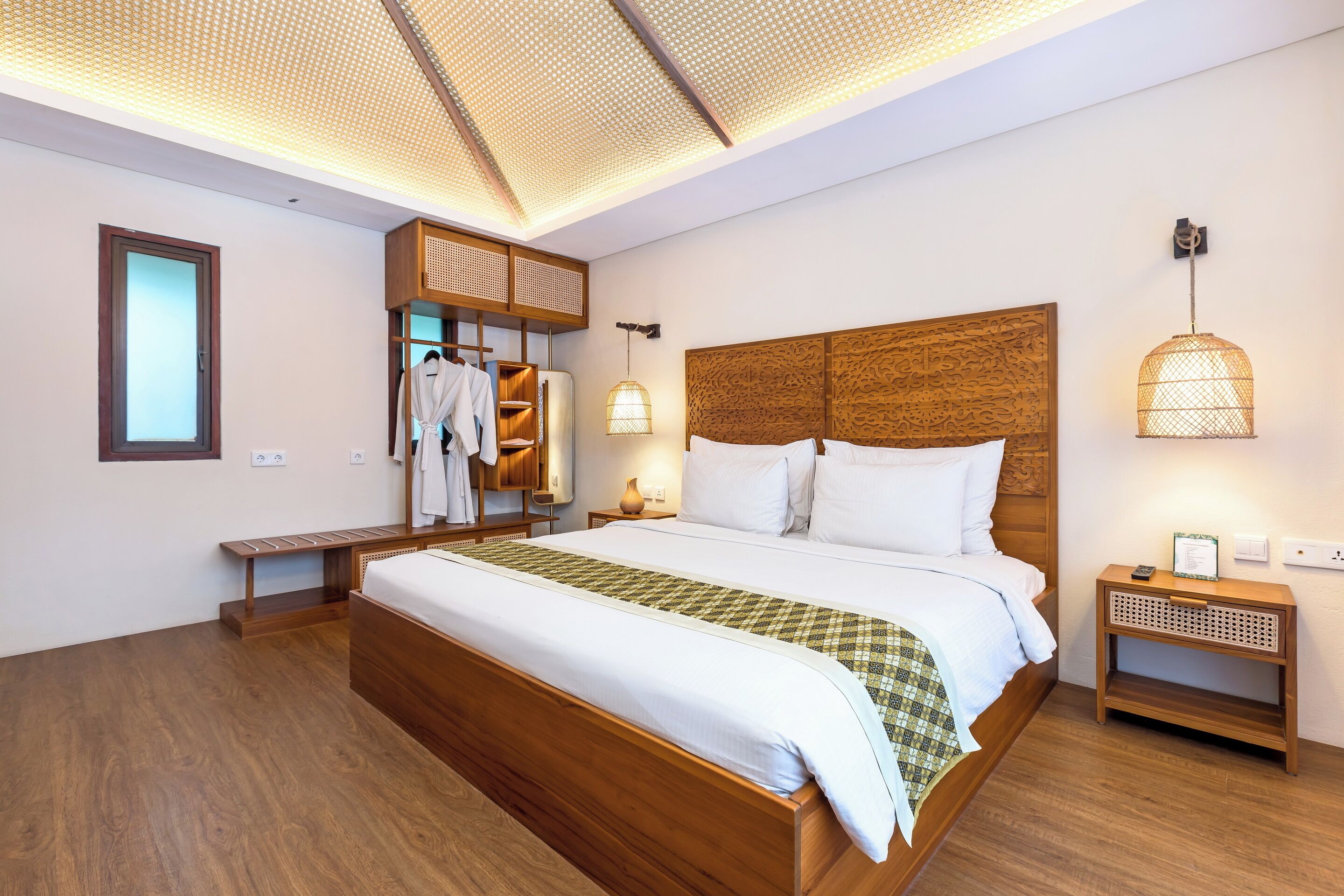Una habitación de hotel moderna con una cama grande, cabecera de madera y un techo con diseño geométrico.
