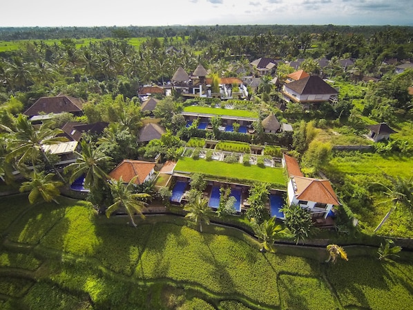 An aerial view of a resort with multiple bungalow-style buildings, lush green fields, and palm trees. - Ubud Green Resort Villas Powered by Archipelago (Ubud)