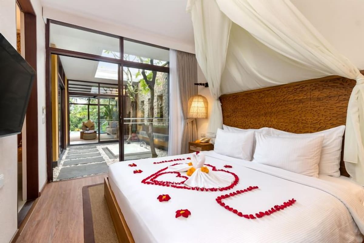 A hotel room with a bed, a television, a nightstand, and a view of a garden through a glass door.