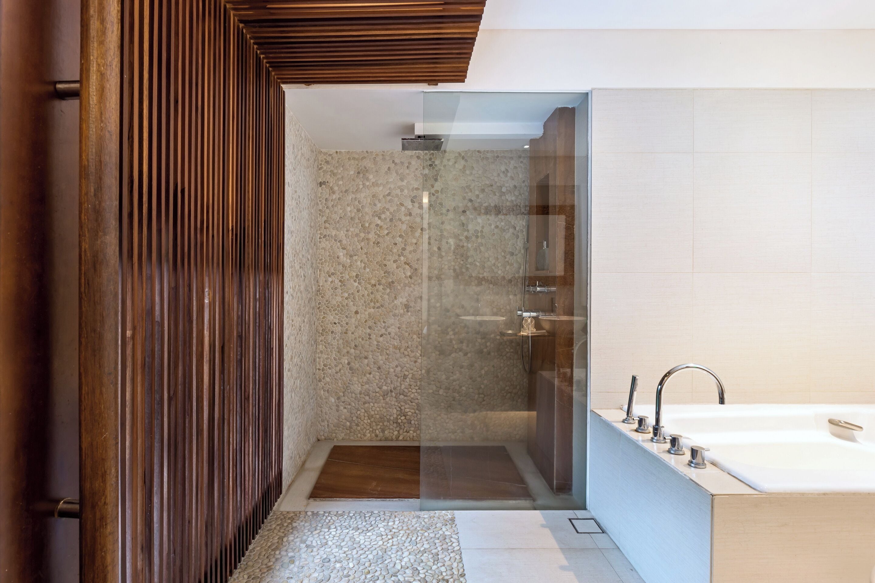 Un baño moderno con ducha envuelta en vidrio, una bañera grande y un diseño de paneles de madera.