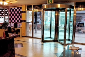 A hotel lobby with a reception desk, a glass elevator, and a view of the outside.
