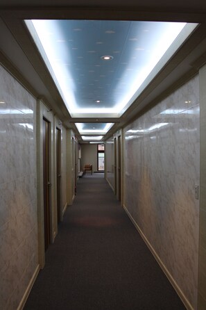 Un long couloir étroit, typique des hôtels, avec un plafond en verrière, des murs en marbre et des portes donnant sur les chambres.