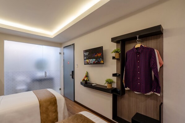 A hotel room with a bed, a wardrobe, a shelf with a poster, and a hanging rack with clothes. - Everyday Hotel Kuta Central (Kuta)
