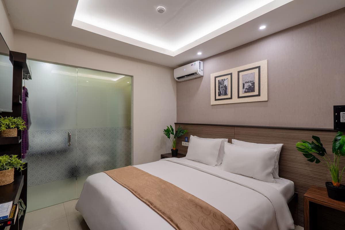 A modern hotel room with a large bed, a glass shower enclosure, and two potted plants.