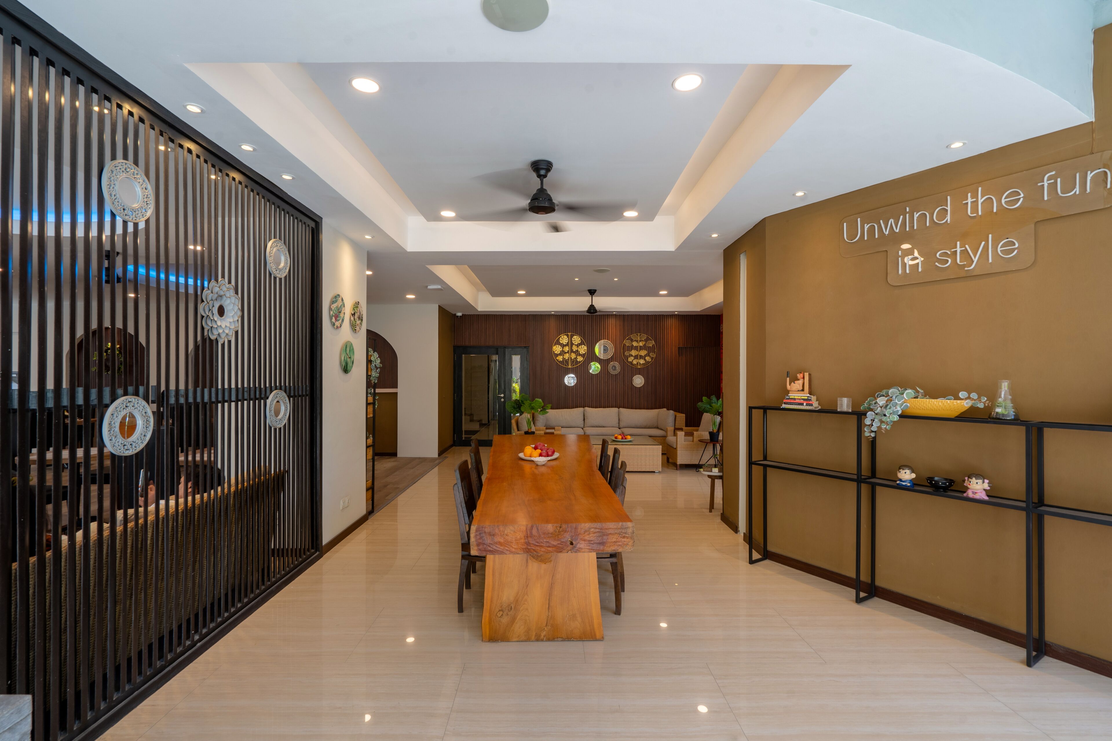 A modern dining area with a wooden table and chairs, a decorative wall with a sign, and a ceiling fan.