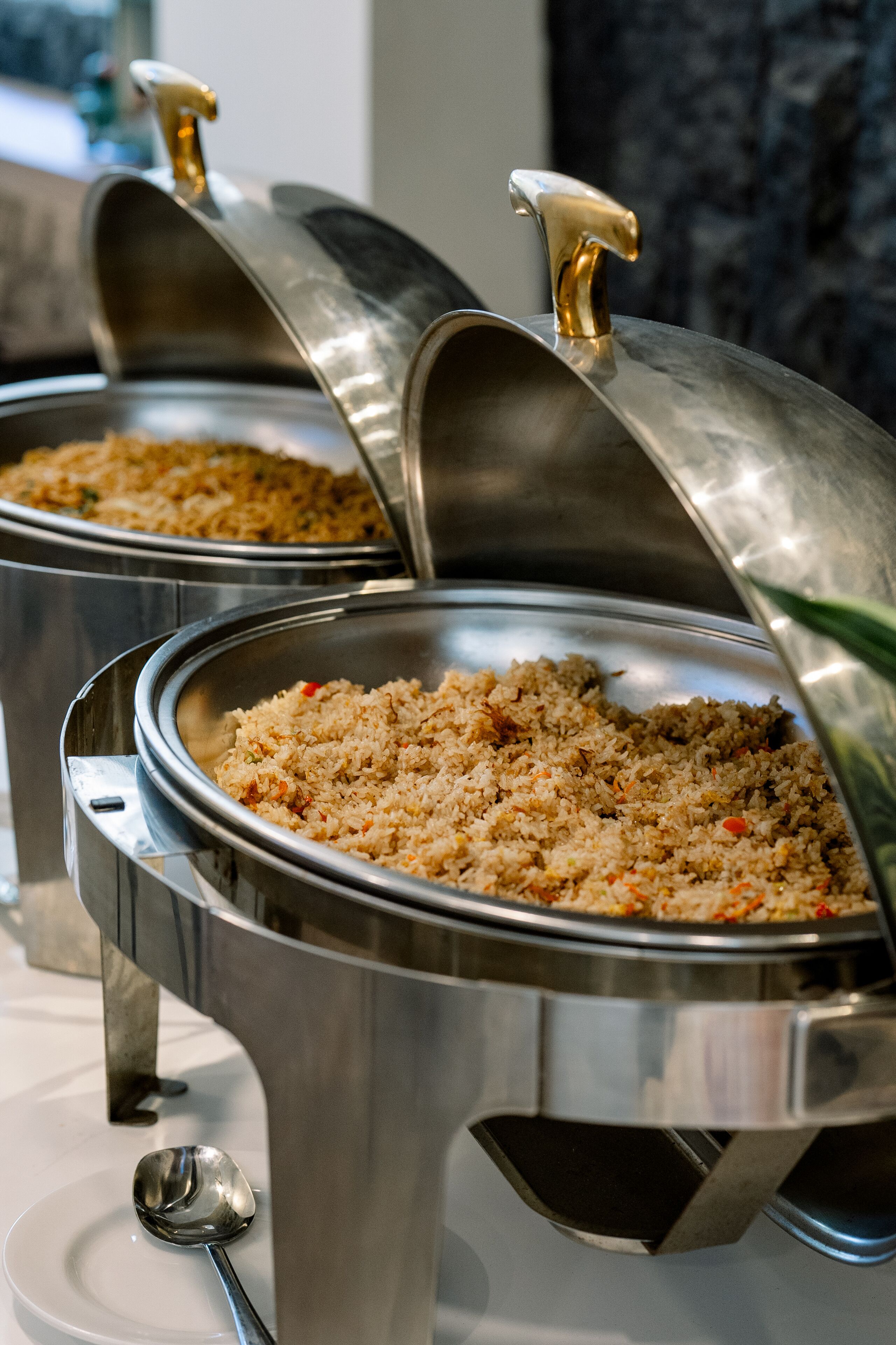 A buffet setup with multiple stainless steel chafing dishes containing food, each with a lid and a ladle.
