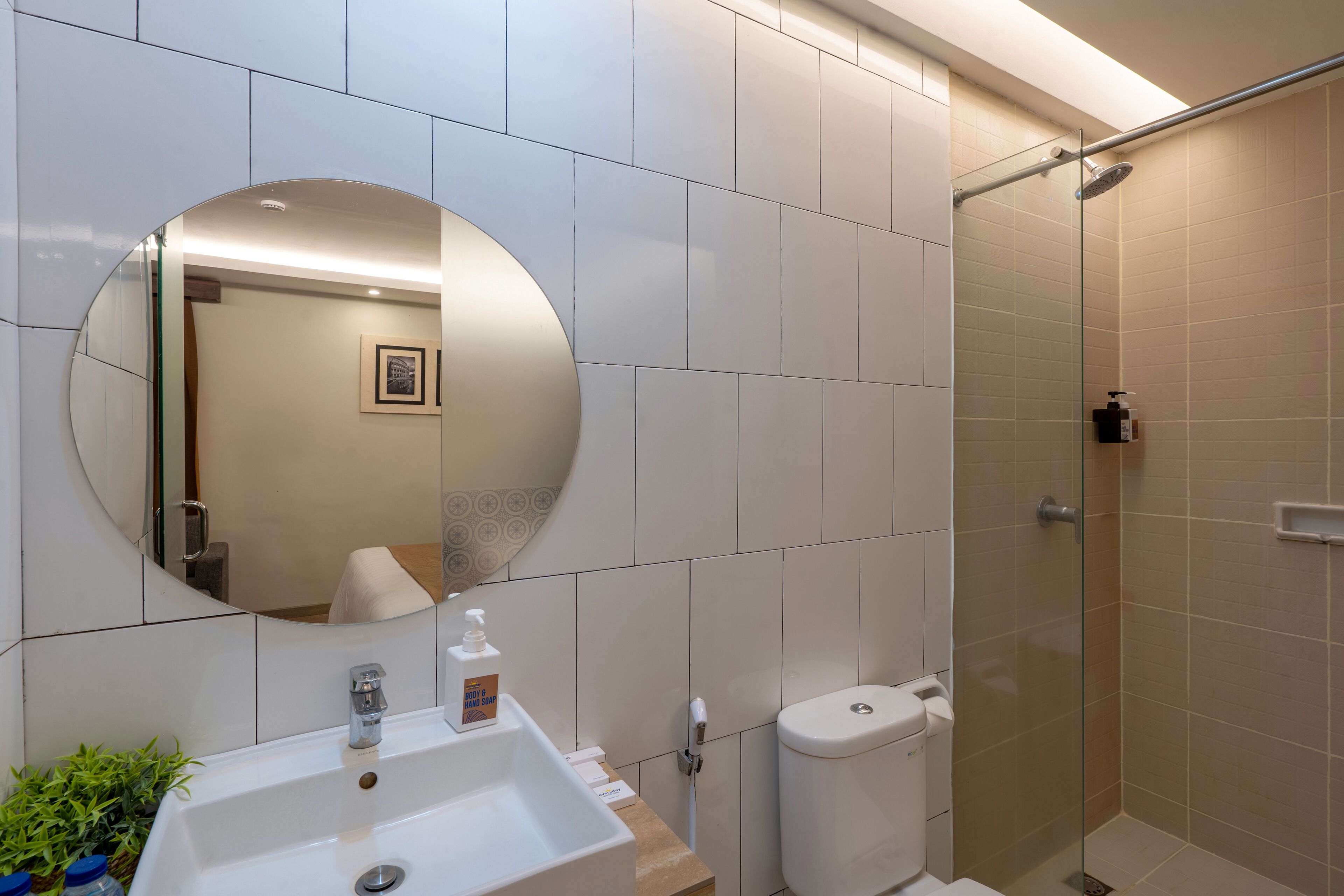 Een moderne badkamer met een ronde spiegel, een wastafel, een toilet en een douche met glazen wanden.