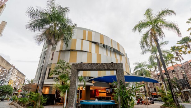 A modern building with a curved facade, a central fountain, and surrounding palm trees. - Everyday Hotel Kuta Central (Kuta)