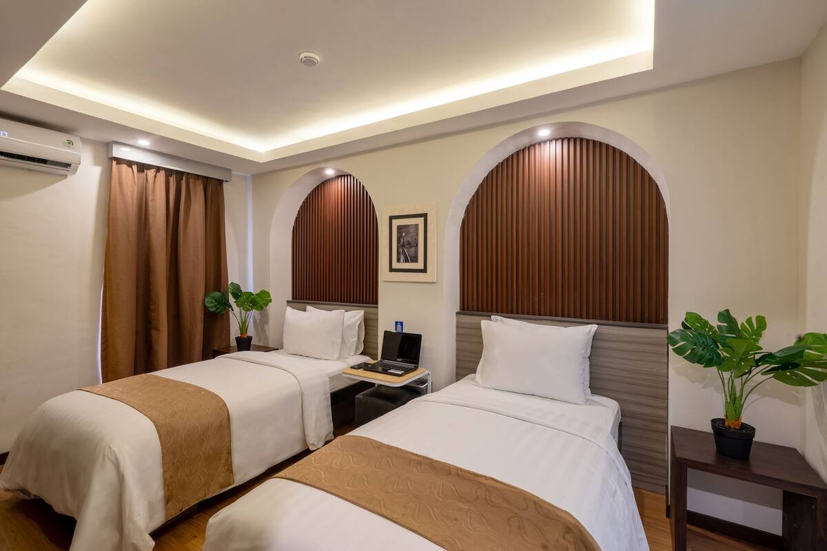A hotel room with two beds, a desk, and a potted plant.