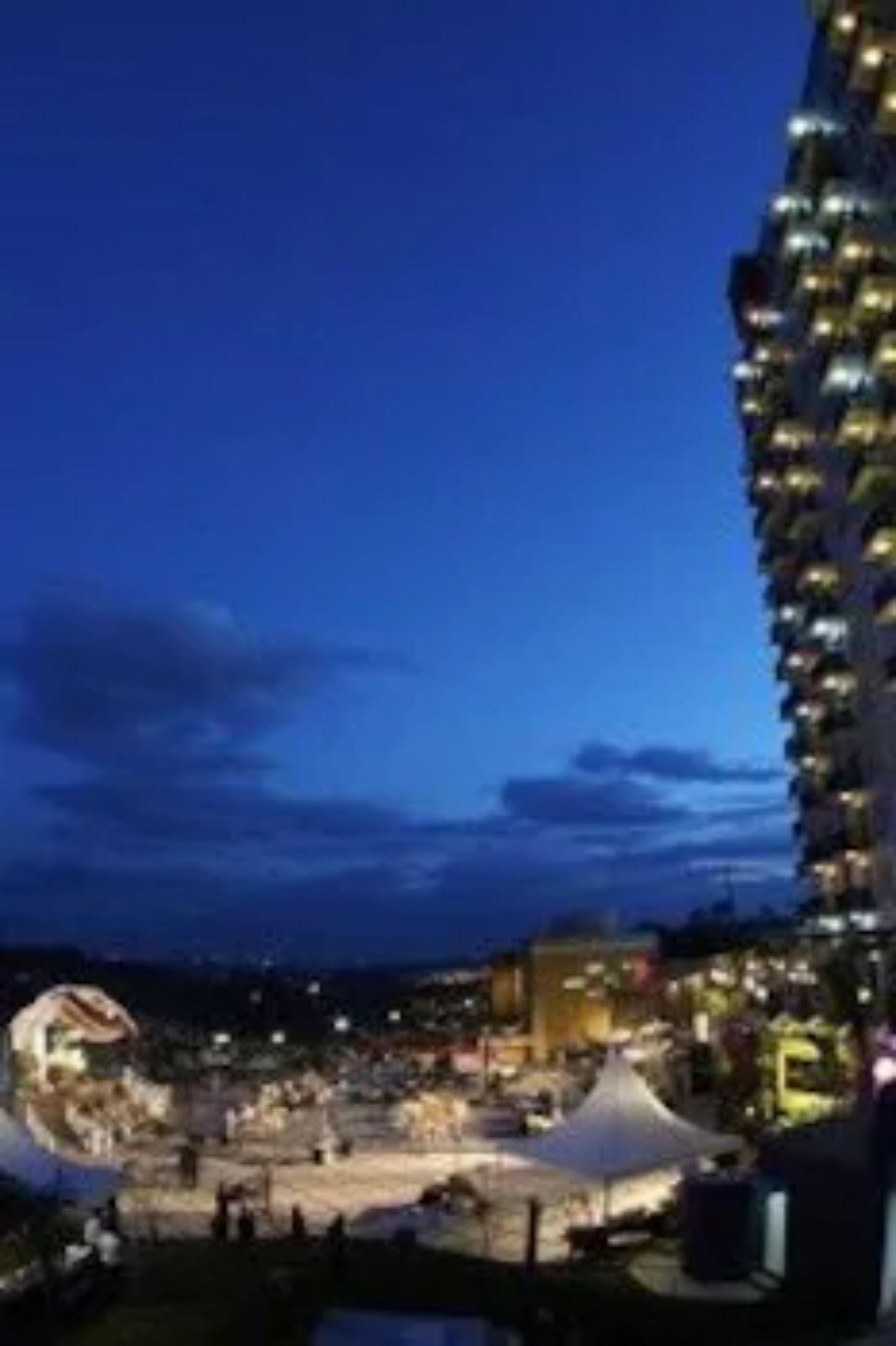 A waterfront hotel with a large building featuring balconies, a central courtyard, and a view of the water.