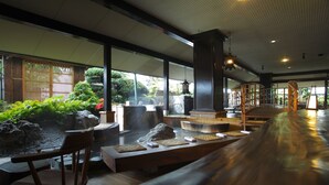 Un interior japonés tradicional con esteras de tatami, muebles de madera y vistas a un jardín a través de amplias ventanas.