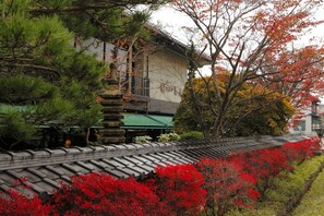 A traditional building with a tiled roof, surrounded by lush greenery and vibrant red foliage. - Hidatei Hanaougi (Takayama)