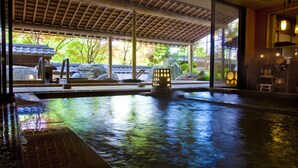 Una piscina interior con techo de estilo japonés, faroles de piedra y vistas a un jardín con rocas y árboles.