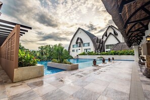 A pool area with a modern building, a clear sky, and a tropical garden.