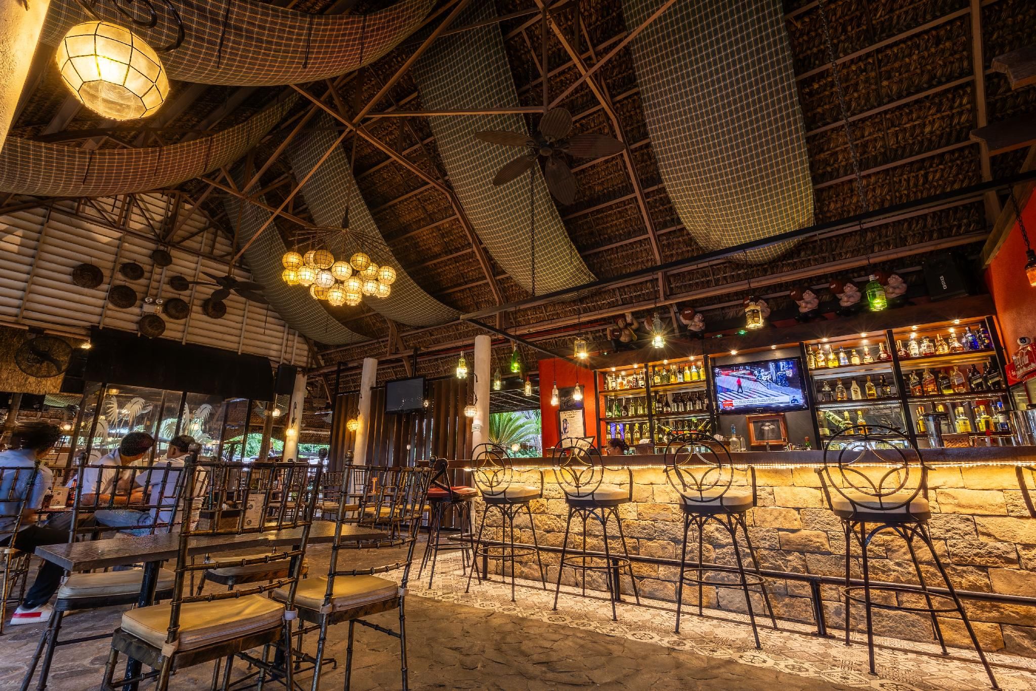 A bar area with multiple seating arrangements, a television screen, and a variety of bottles on shelves.