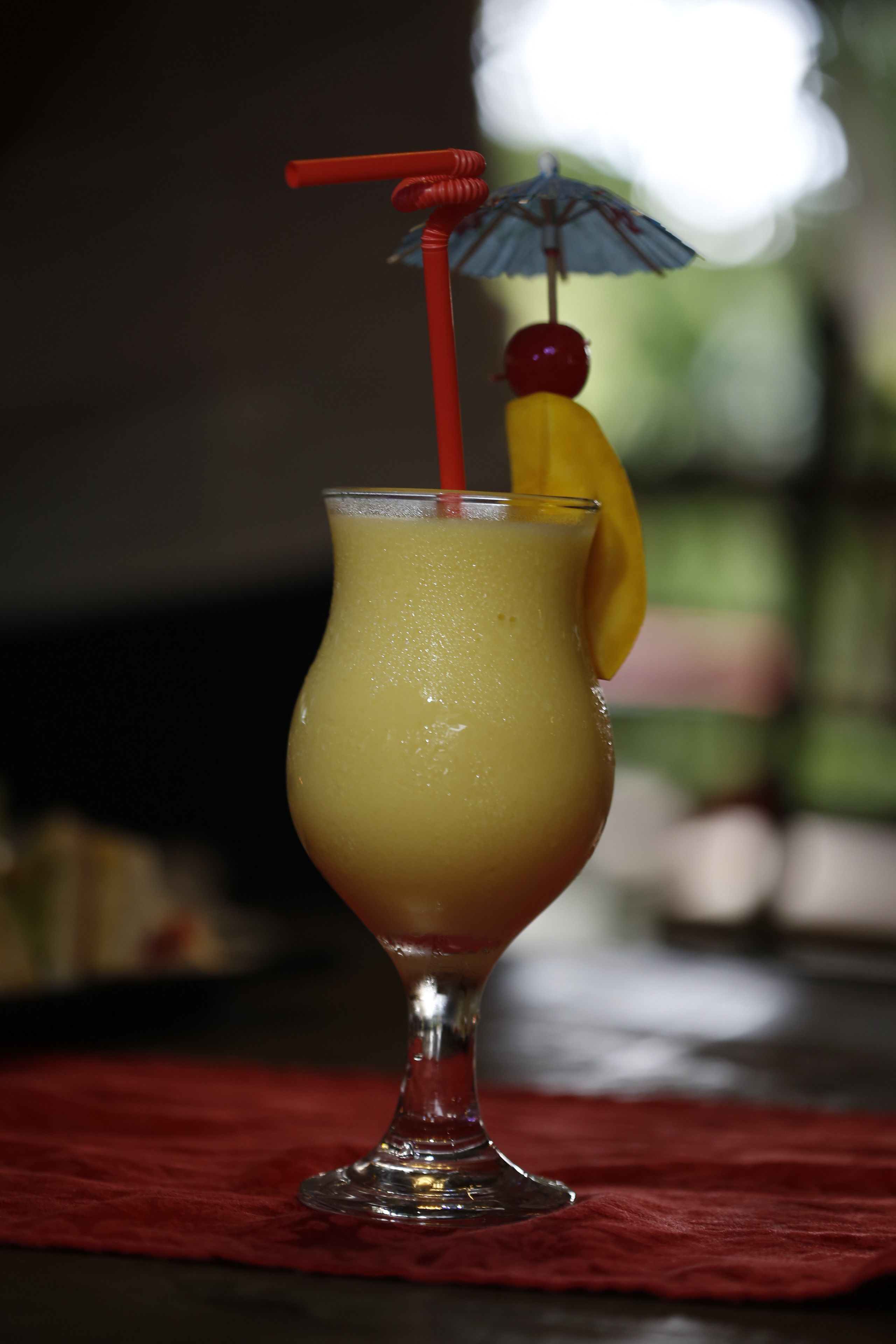 A cocktail in a glass with a red straw and a small umbrella, placed on a red cloth.