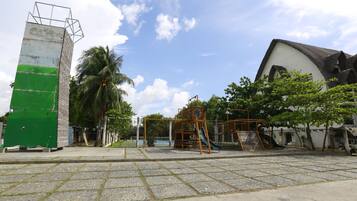 Explore the outdoor playground with a slide and swings, surrounded by lush trees and a charming building.