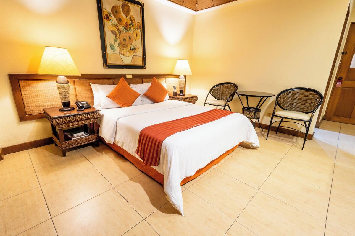 A hotel room with a bed, two bedside tables with lamps, a chair, and a painting on the wall.