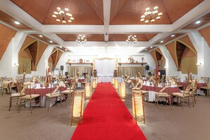 A banquet hall with a red carpet aisle, wooden chairs, and chandeliers.