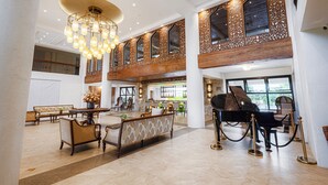 A spacious lobby with a grand piano, seating arrangements, and a chandelier.