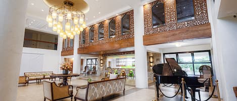A spacious lobby with a grand piano, seating arrangements, and a chandelier.