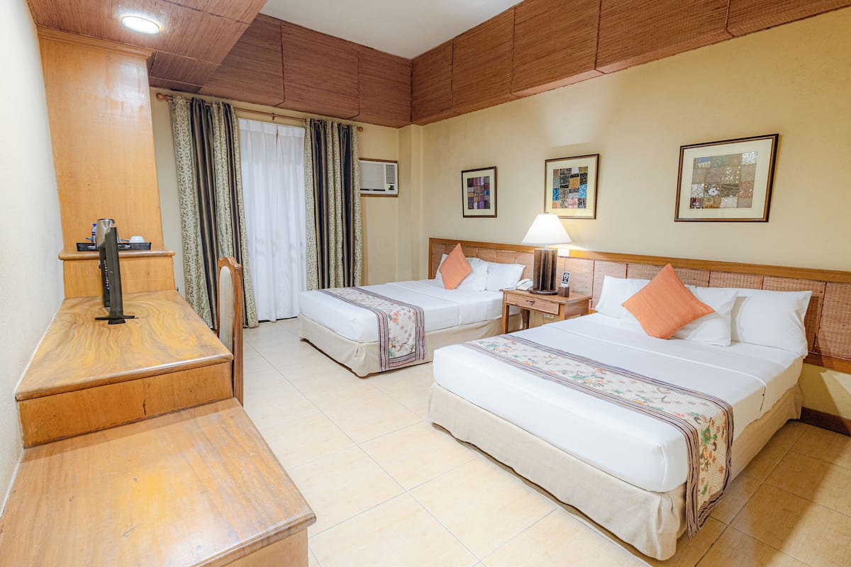 A hotel room with two beds, a desk, a chair, a lamp, and artwork on the walls.