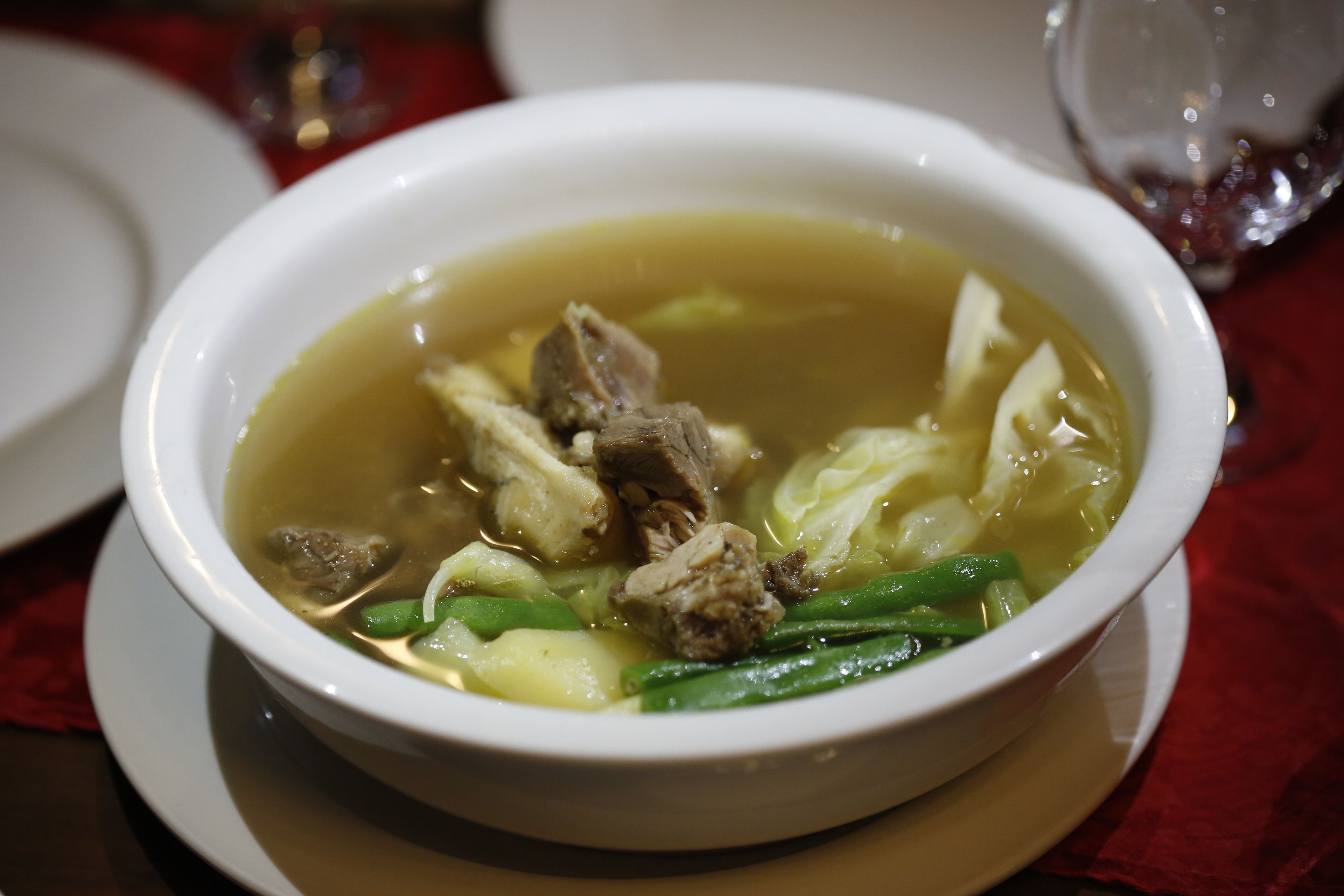 A bowl of soup with meat and vegetables on a white plate.