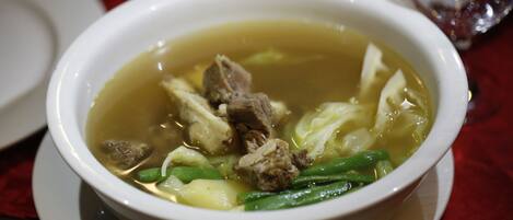 A bowl of soup with meat and vegetables on a white plate.