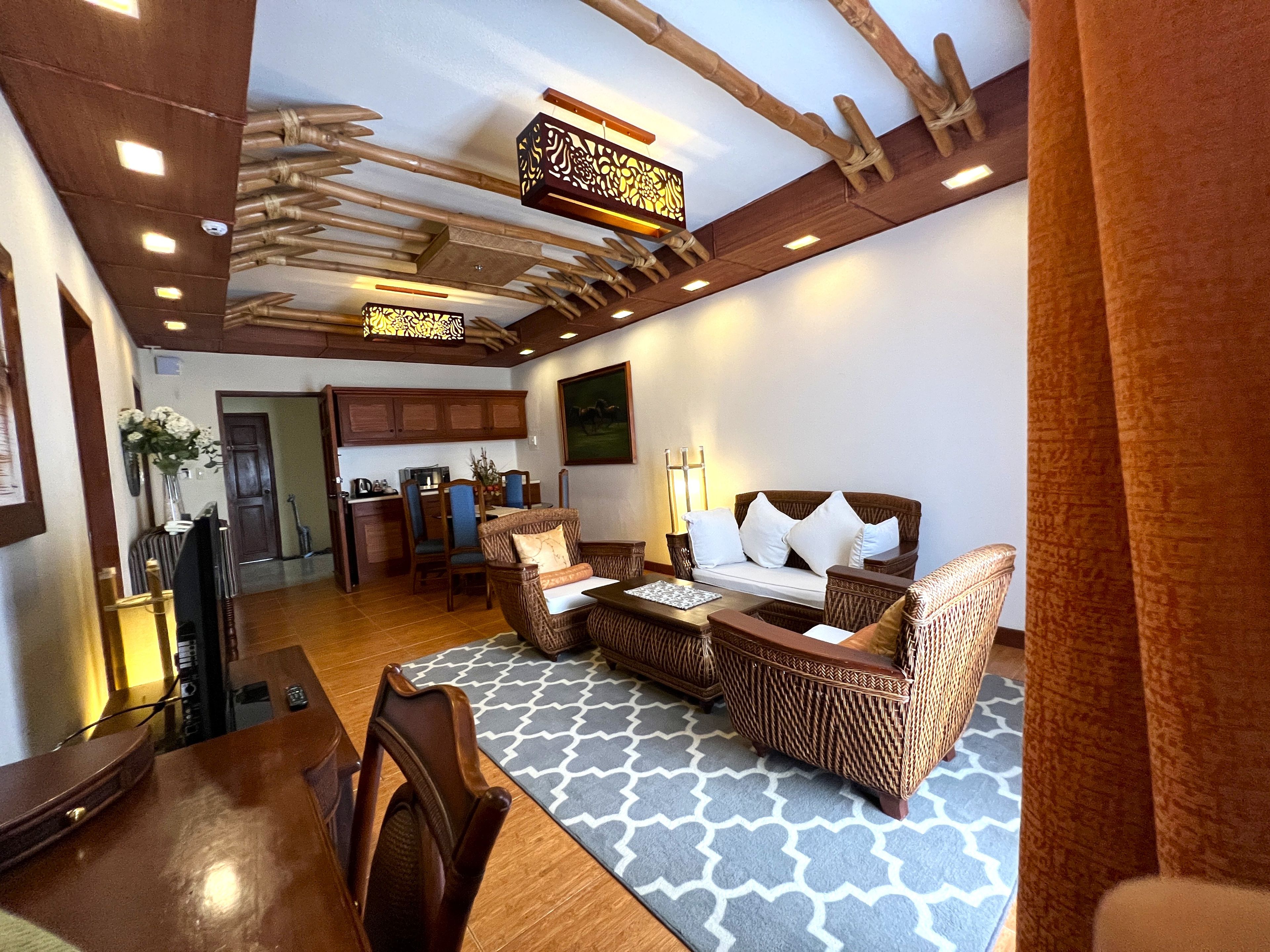 A room with a sofa, chairs, a dining table, and a kitchen area in the background.
