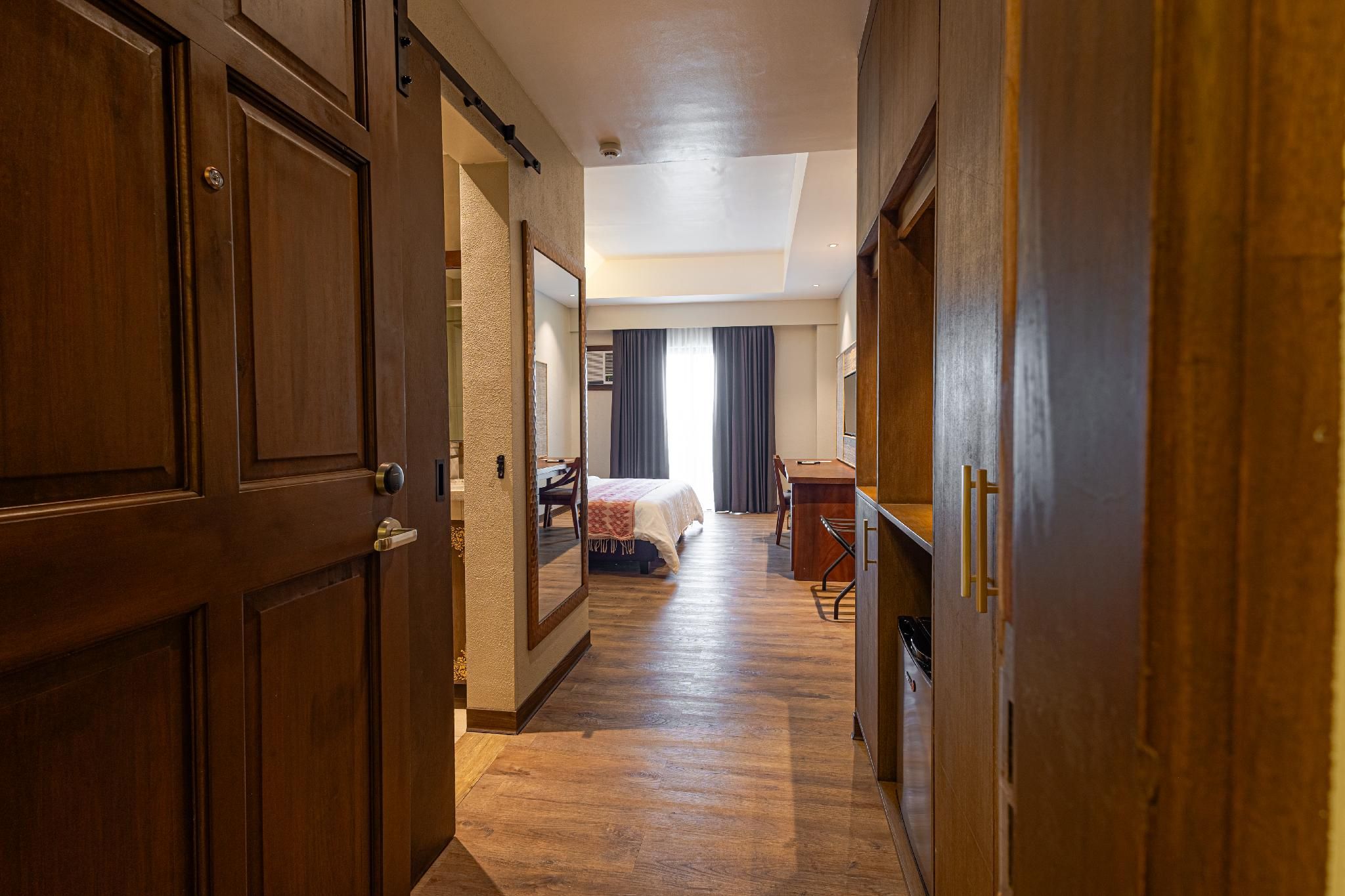 A hotel hallway with wooden doors, a bed, a desk, and a chair.