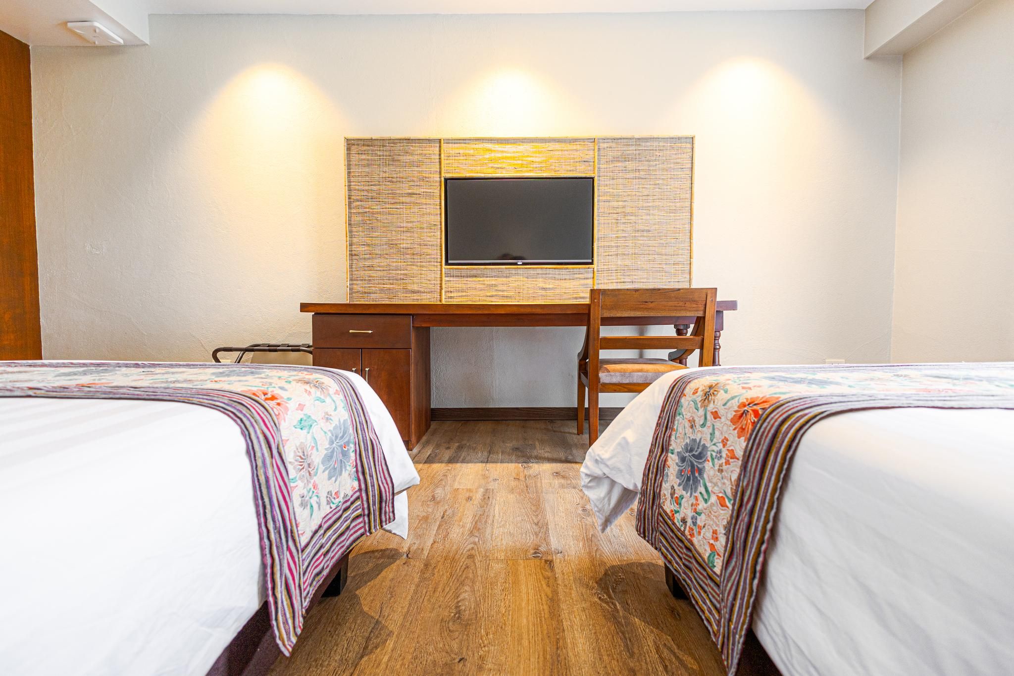 A hotel room with two beds, a desk, and a television.