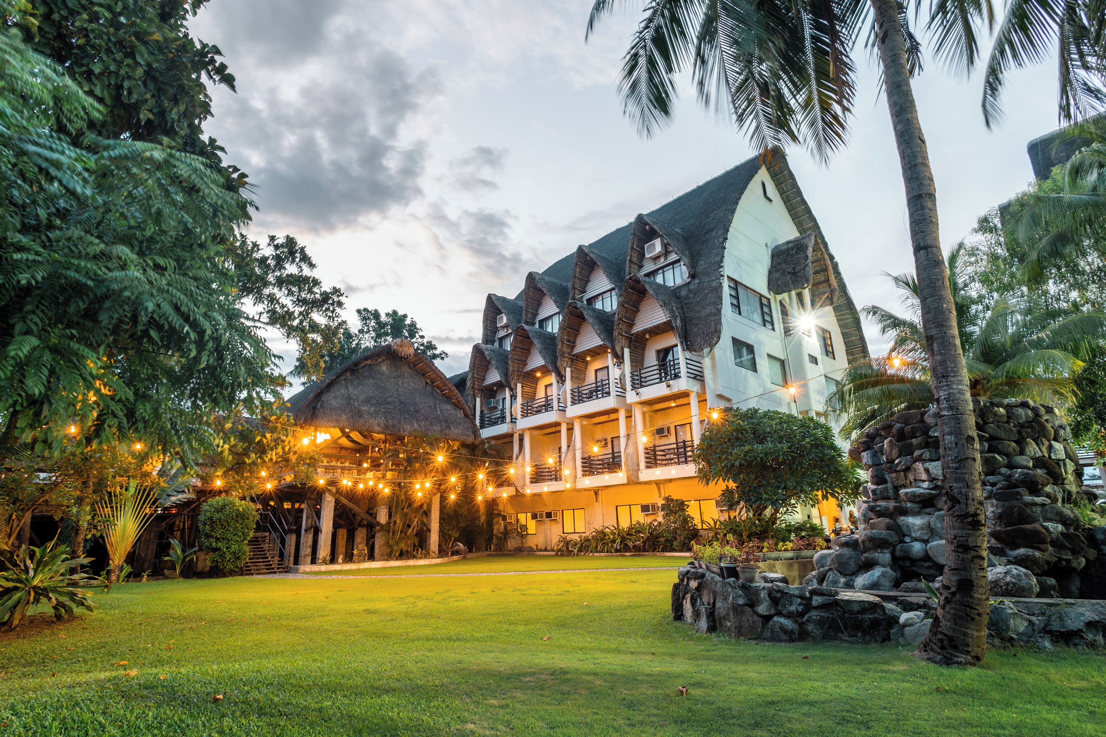 A resort with a thatched-roof building, a well-maintained lawn, and a stone wall.