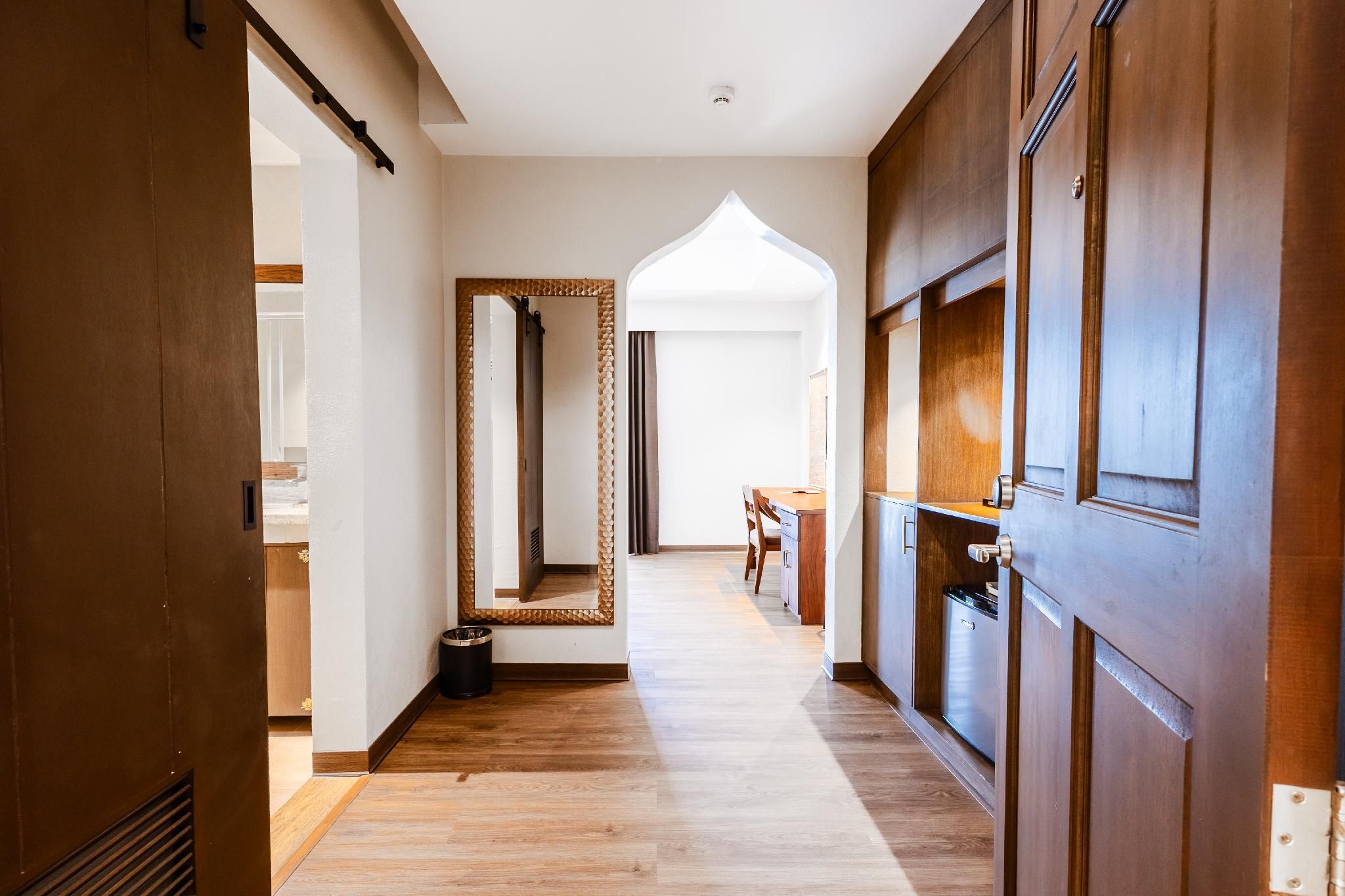 A hallway with wooden flooring, a large mirror, and a door with a handle.