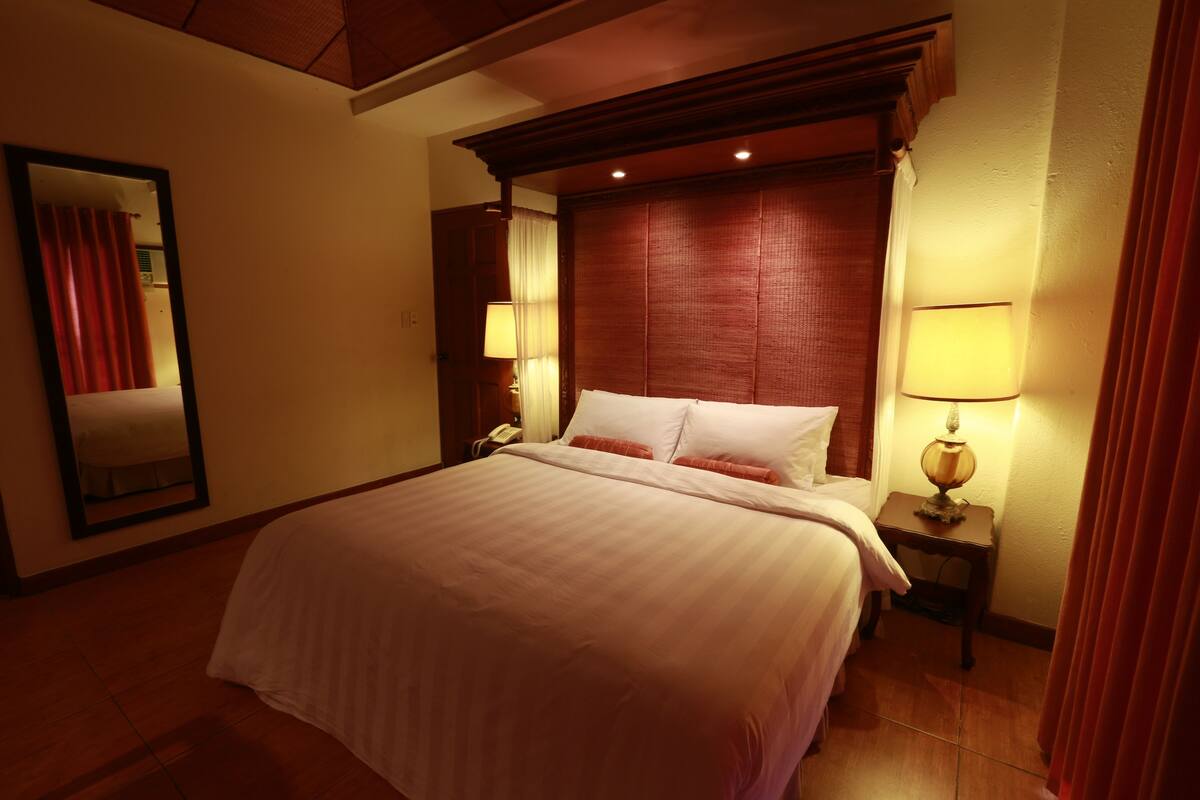 A hotel room with a large bed, wooden headboard, bedside lamps, and a mirror on the wall.