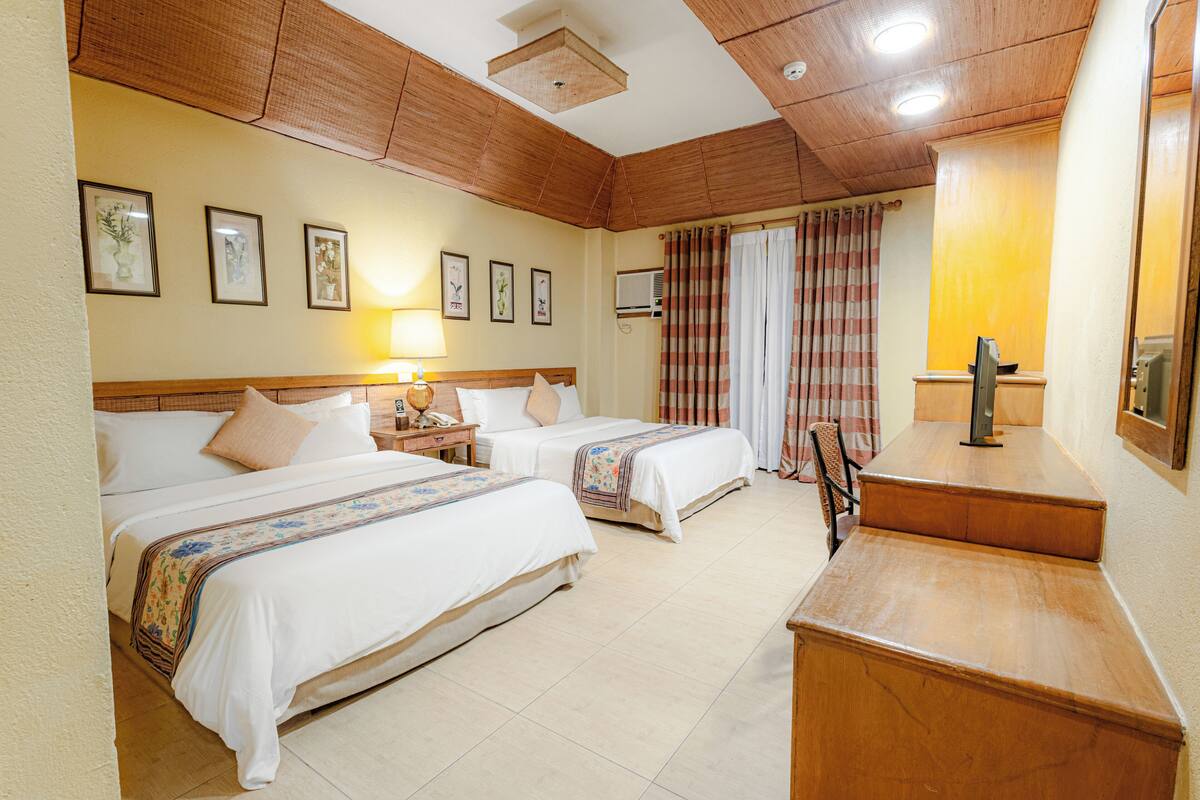 A hotel room with two beds, a desk, a chair, a TV, and a window with curtains.