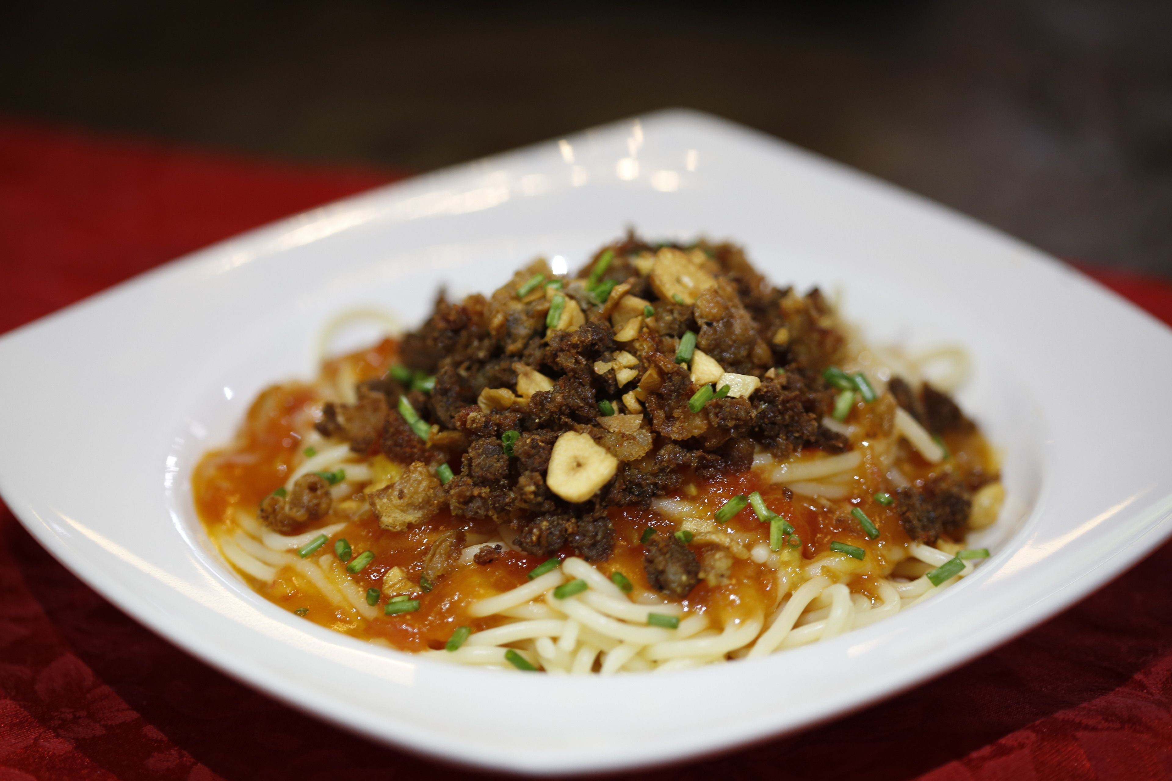 Une assiette de spaghettis recouverte d’une sauce à base de viande et garnie d’oignons verts.