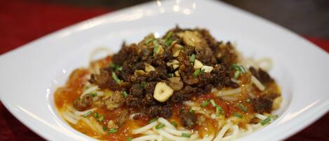 Une assiette de spaghettis recouverte d’une sauce à base de viande et garnie d’oignons verts.