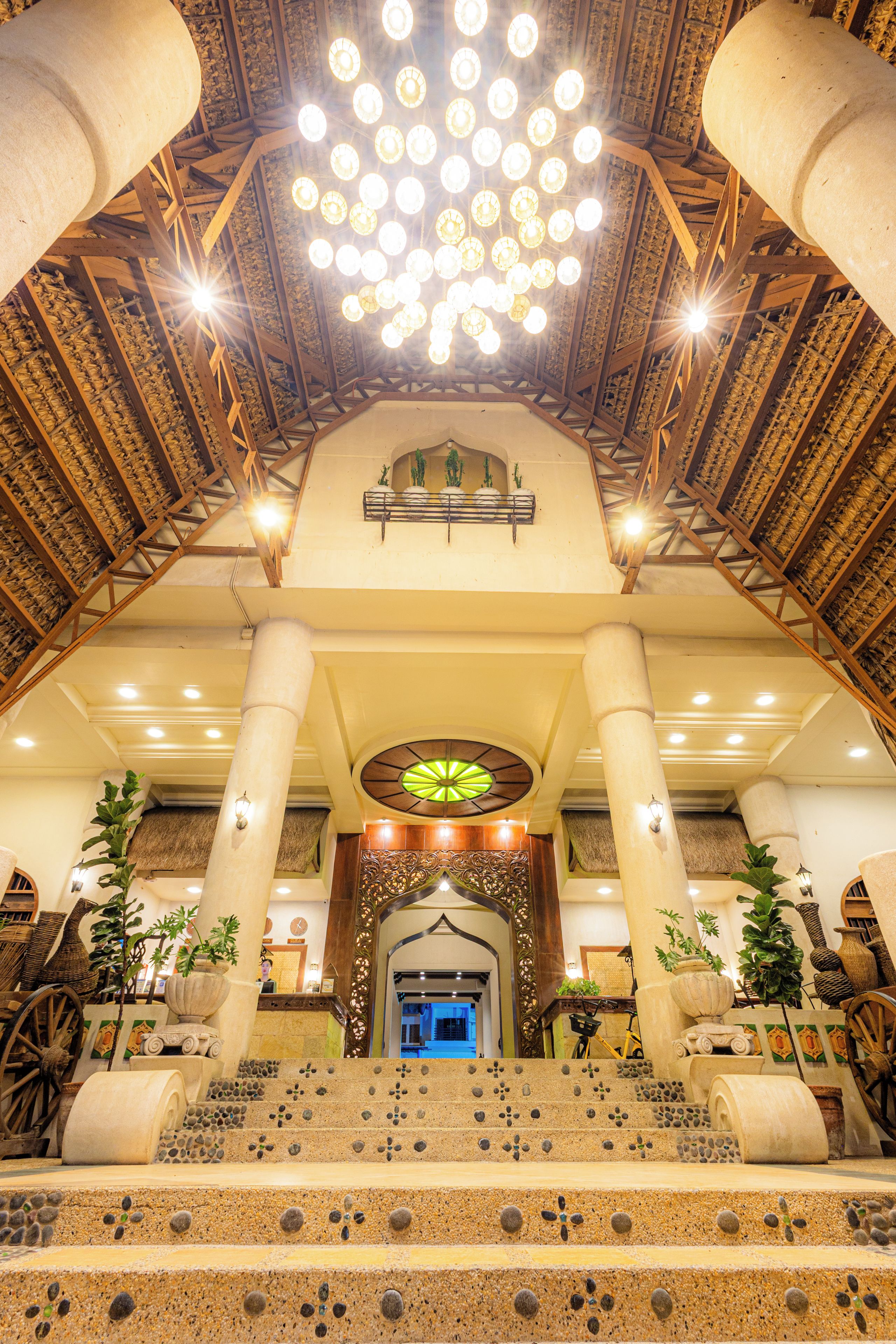 A grand lobby with a high ceiling, ornate columns, and a central staircase leading to an upper level.
