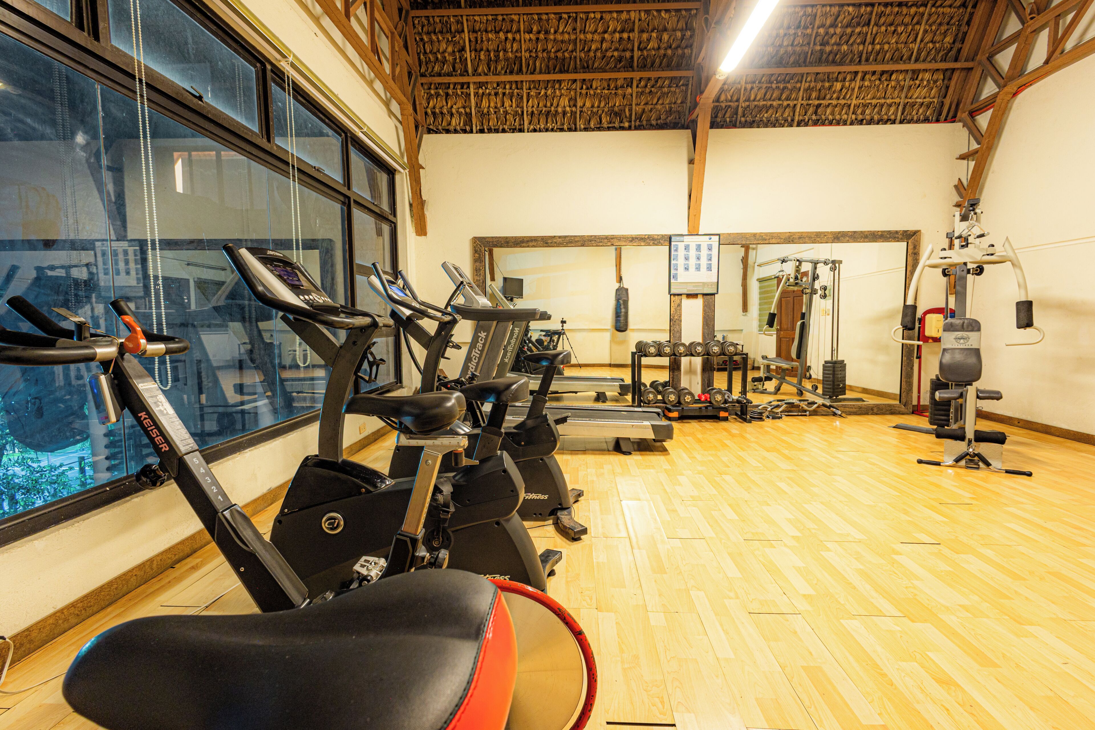 Un gimnasio con equipo de ejercicio, ventanas amplias y piso de madera.