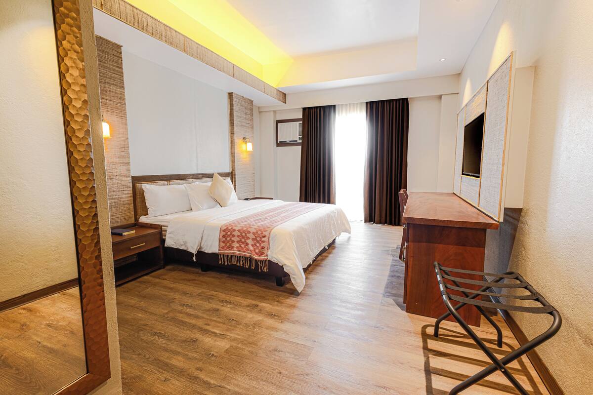 A hotel room with a bed, bedside table, chair, and a desk with a flat-screen TV.