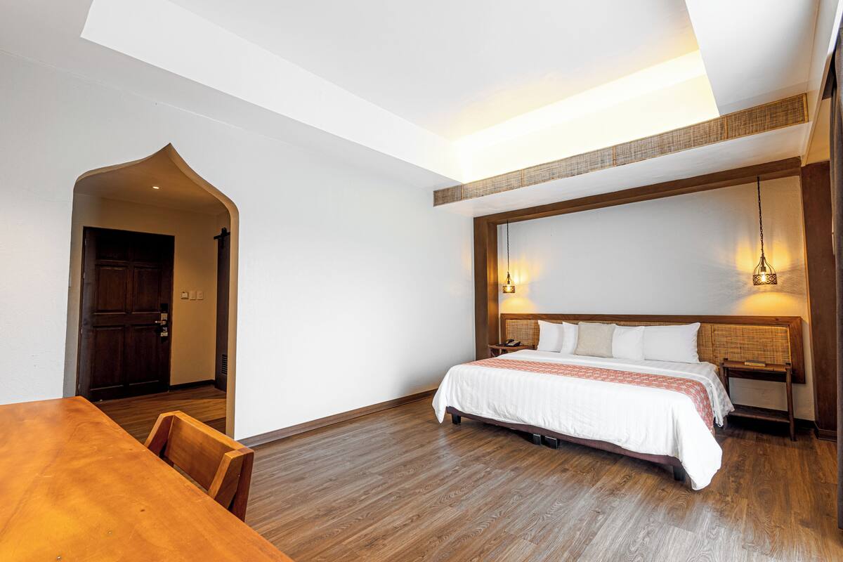 A bedroom with a wooden floor, a bed with white bedding, a wooden nightstand, and two wall-mounted lamps.