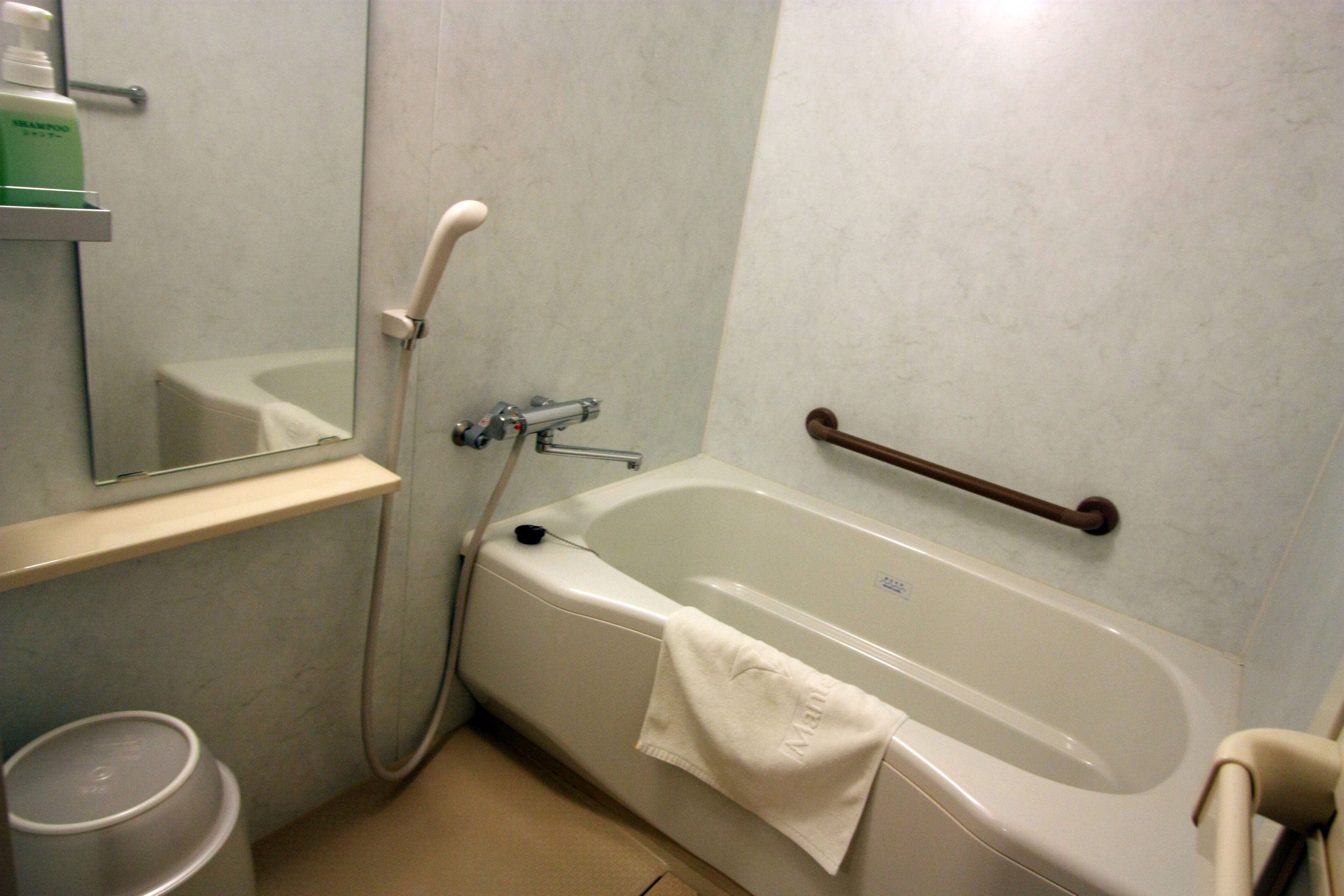 Un baño con bañera, barra de apoyo, espejo y estante con artículos de aseo.