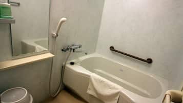 Un baño con bañera, barra de apoyo, espejo y estante con artículos de aseo.