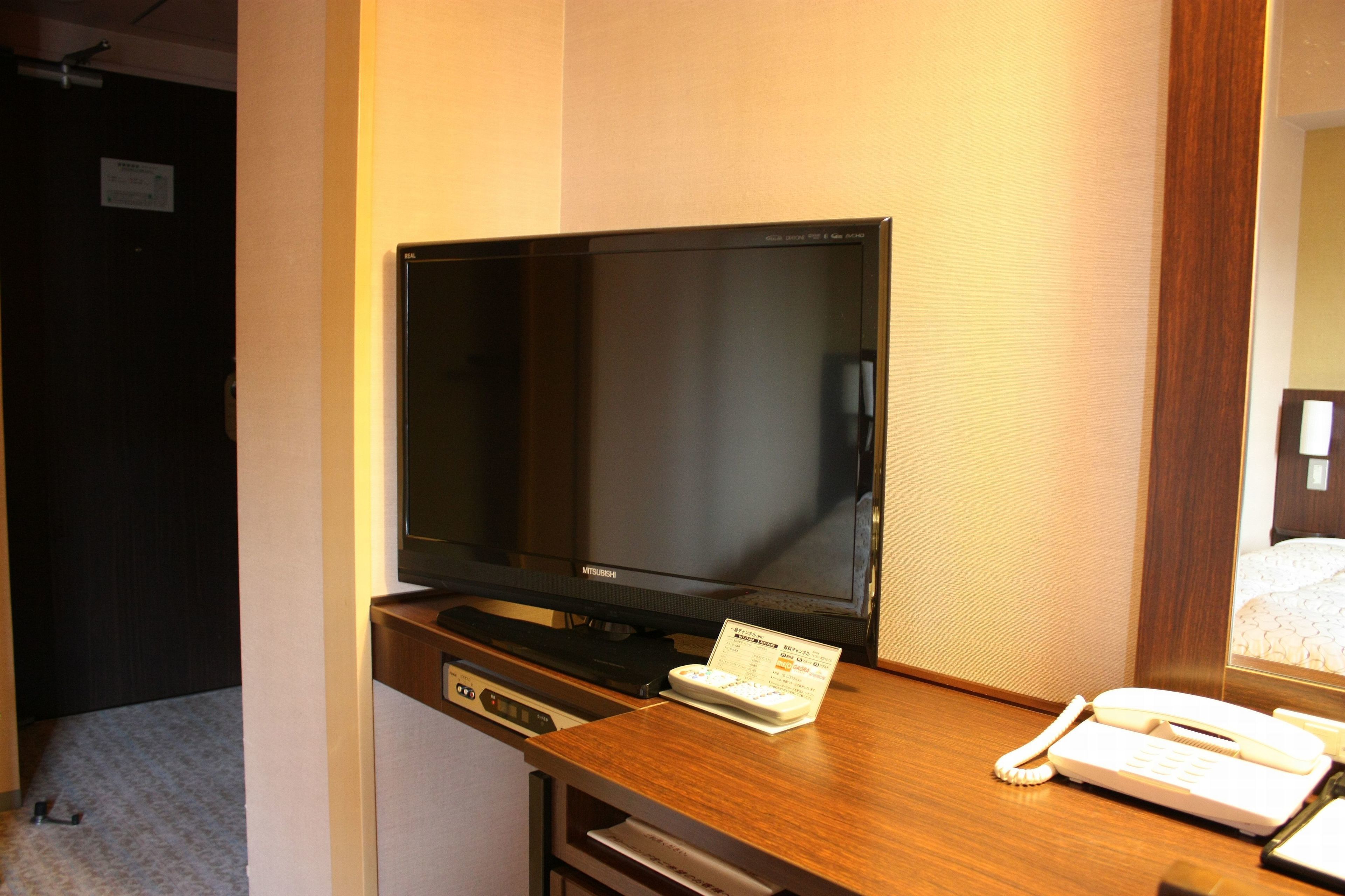 Una habitación de hotel con una televisión de pantalla plana sobre un escritorio de madera, un teléfono y una tarjeta pequeña en el escritorio.