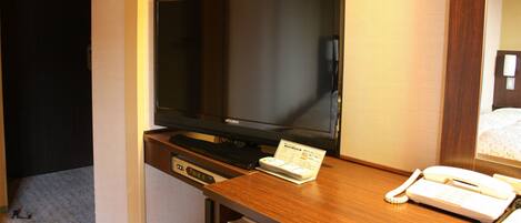 Una habitación de hotel con una televisión de pantalla plana sobre un escritorio de madera, un teléfono y una tarjeta pequeña en el escritorio.