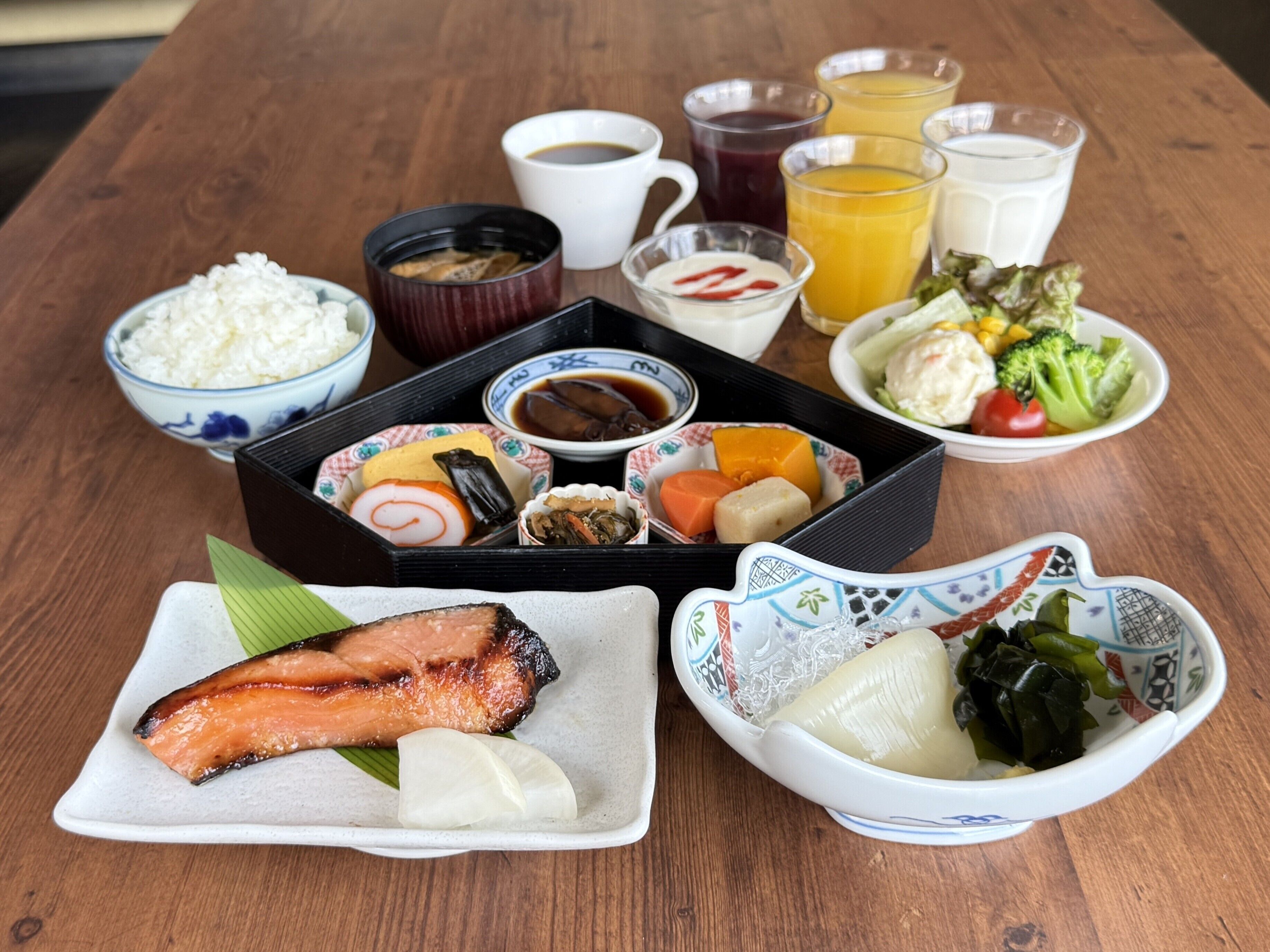 Eine traditionelle japanische Mahlzeit mit Reis, Fisch, Gemüse und verschiedenen Beilagen auf einem Holztisch.